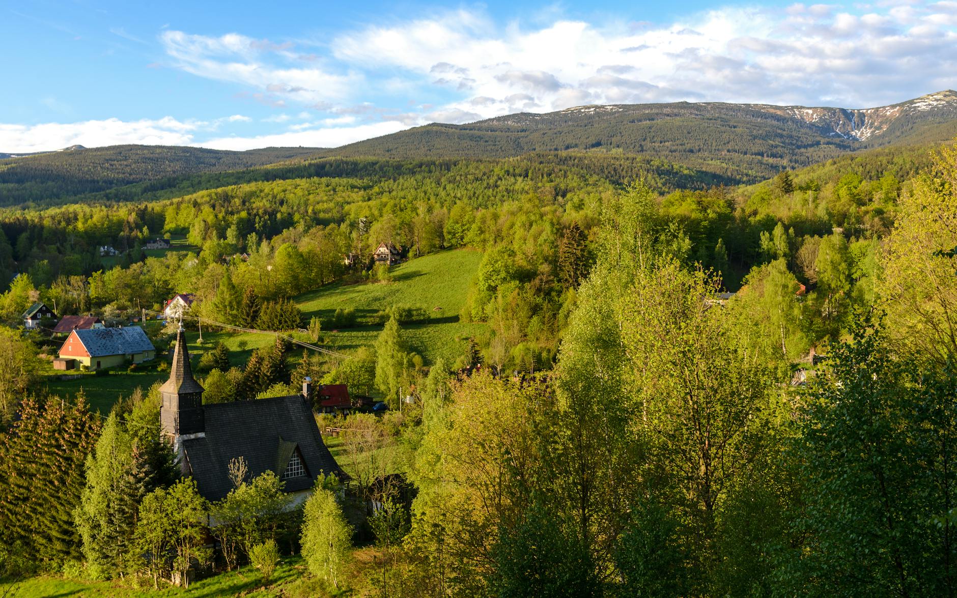 Widok na Karpacz z górami Karkonoszami w tle podczas słonecznego dnia, z zielenią i pierwszymi oznakami wiosny.